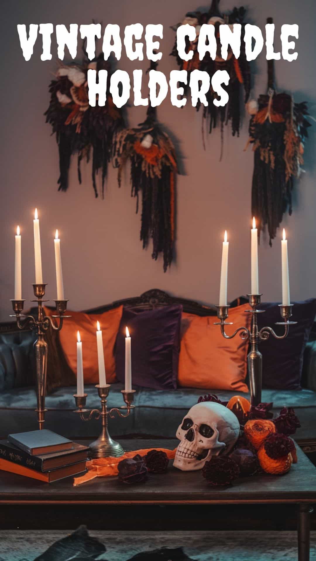 A photo of a modern and elegant Halloween living room with vintage candelabras, flickering candles, antique books, and moody dried florals. There is a couch with orange and purple cushions and a coffee table with a skull. On the wall, there are hanging dried florals and a vintage candelabra. The room has a moody atmosphere with a soft orange hue.