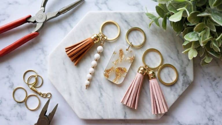 Handmade tassel and charm keychains arranged on a marble background with gold hardware and greenery